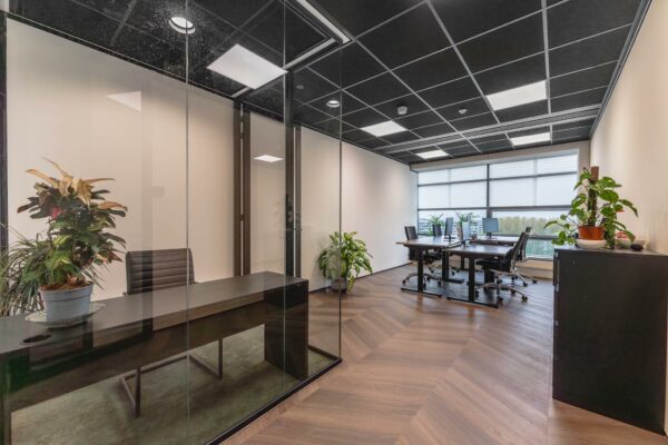 Modern kantoorinterieur aan de Joop Geesinkweg met glazen vergaderruimte, bureaus en groene kamerplanten.